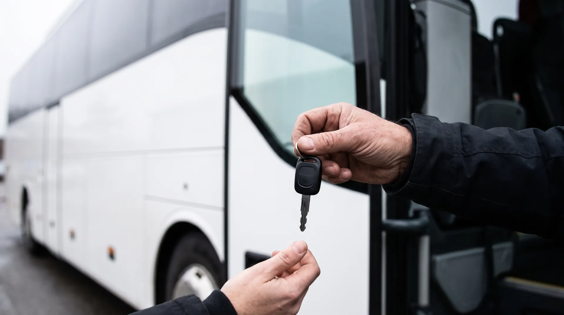 En hand lämnar över en bussnyckel vid dörren till en vit turistbuss